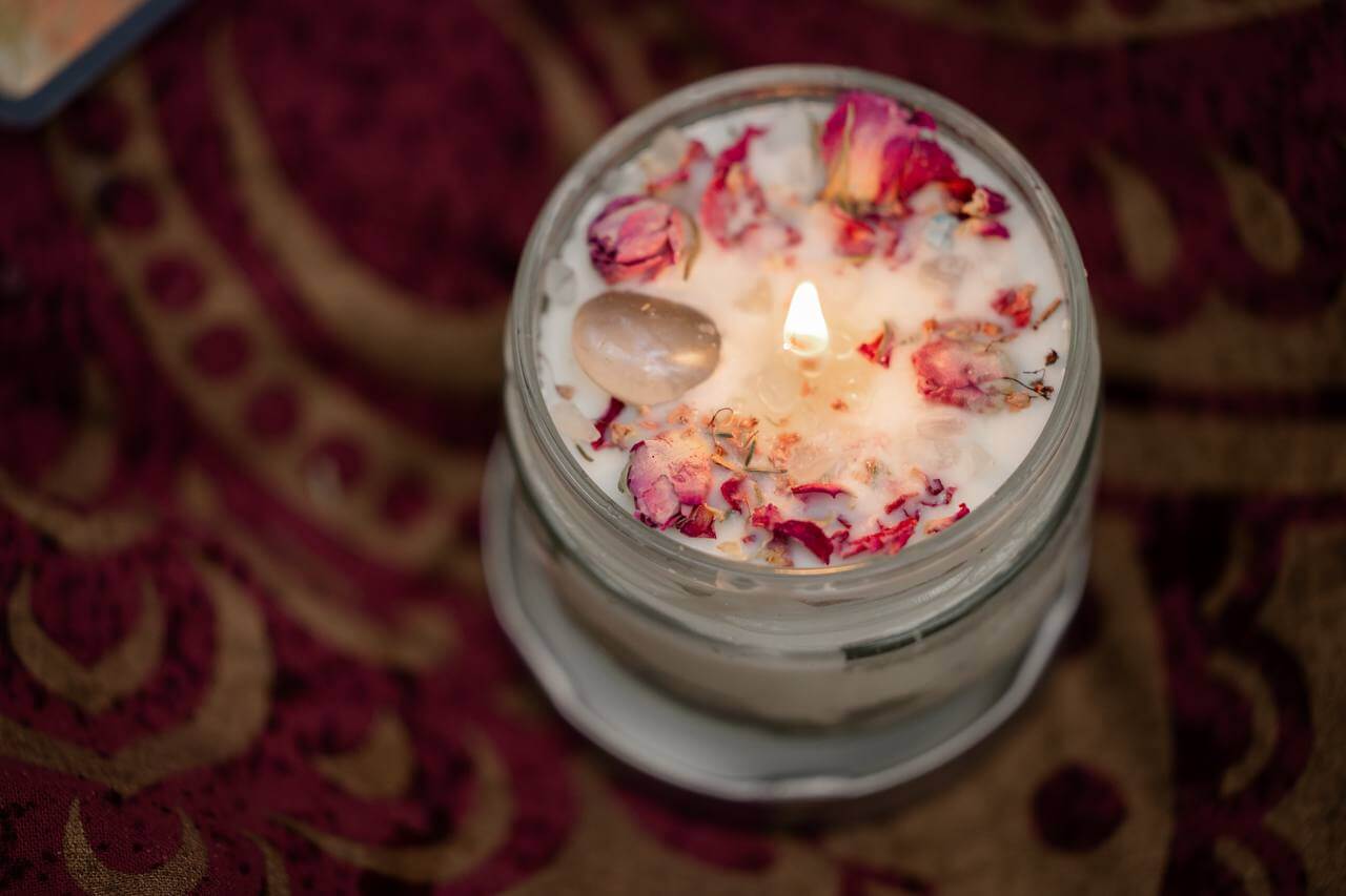 Ritualkerze, die brennt, erstellt mit Rosenblüten, ätherischen Ölen und Steinen von Expertin Tina Wasem.